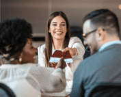 A woman handing visa documents and a passport to a smiling couple at an office desk, representing visa or travel services